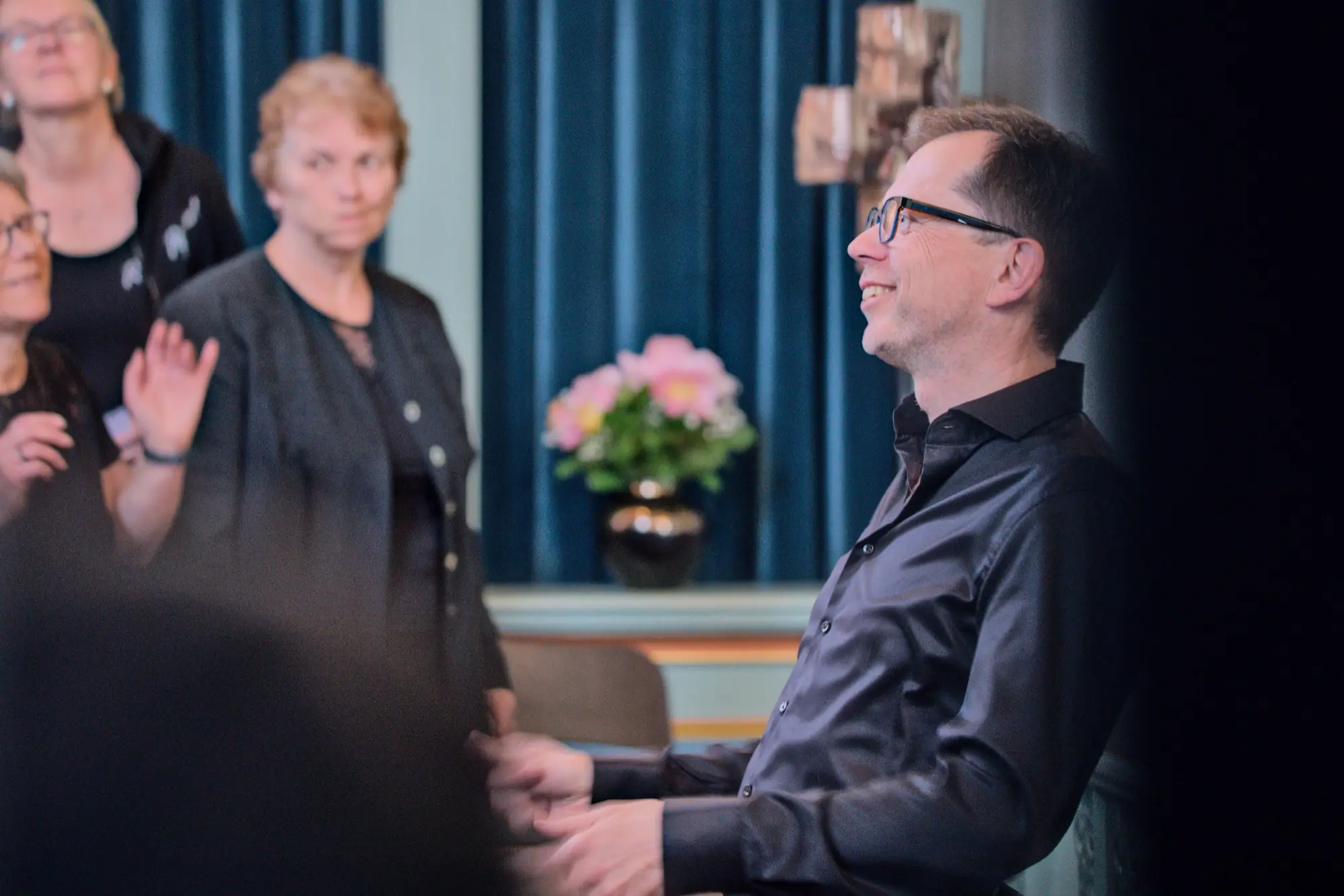 Schnappschuss auf den Kantor Thomas Wächter mit schwarzem Hemd sitzend im Altarraum im Hintergrund sieht man eine Sängerin des Gospelchor Rejoice 