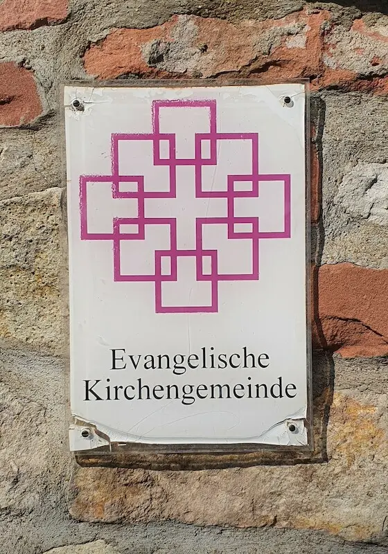 Ein Schild an der Mauer der Kirche in Middelhagen auf Rügen zeigt das Facettenkreuz der Evangelischen Kirche. 