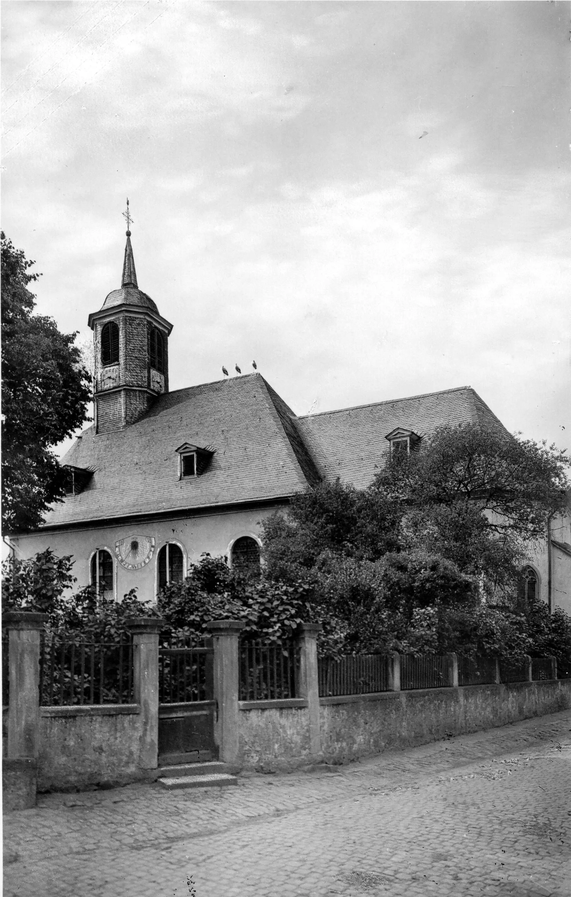 Kirche an der Einmündung der Kirchstraße mit der Einfriedigung bis 1960 und drei Störchen auf dem Dach!