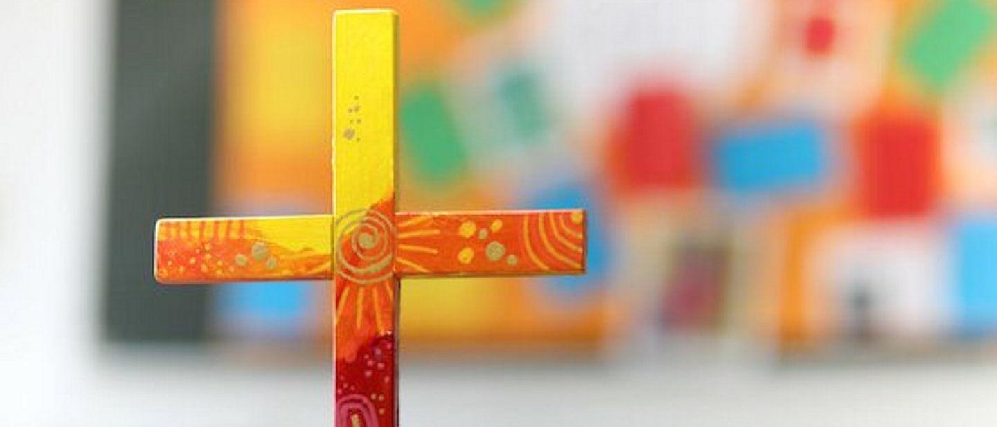 buntes Holzkreuz auf Tuch auf einem Tisch.