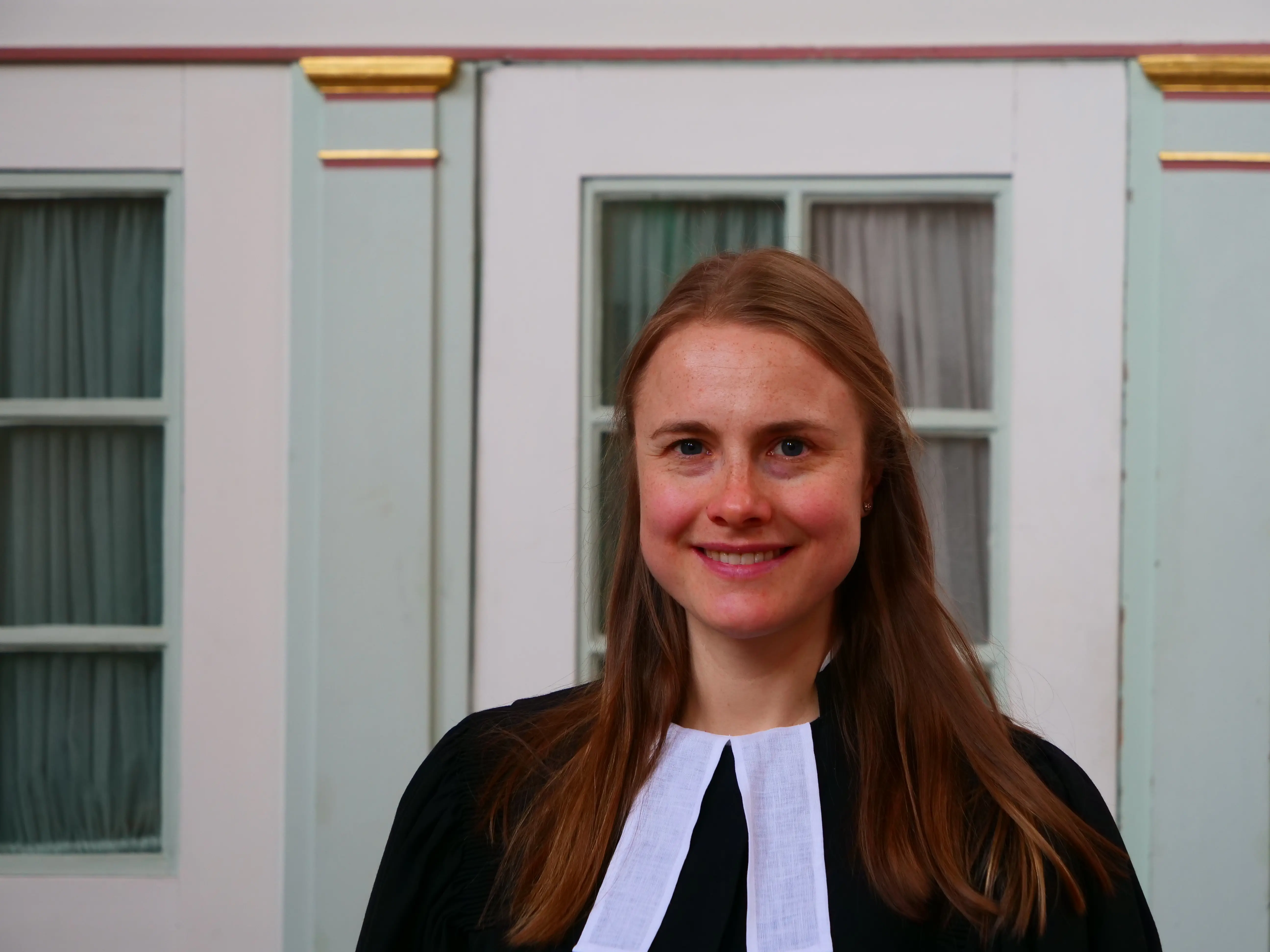 Vikarin Miriam Wolf im Talar in der Ev. Kirche Liederbach vor einer Tür.
