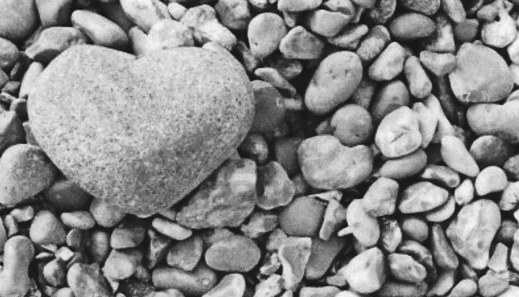 Das Foto zeigt einen großen Stein in Herzform der auf vielen kleineren Steinen liegt.